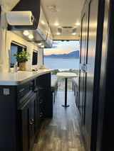 Inside a cozy rv rental with a modern kitchenette, dining table, and stunning sunset lake & mountain views.