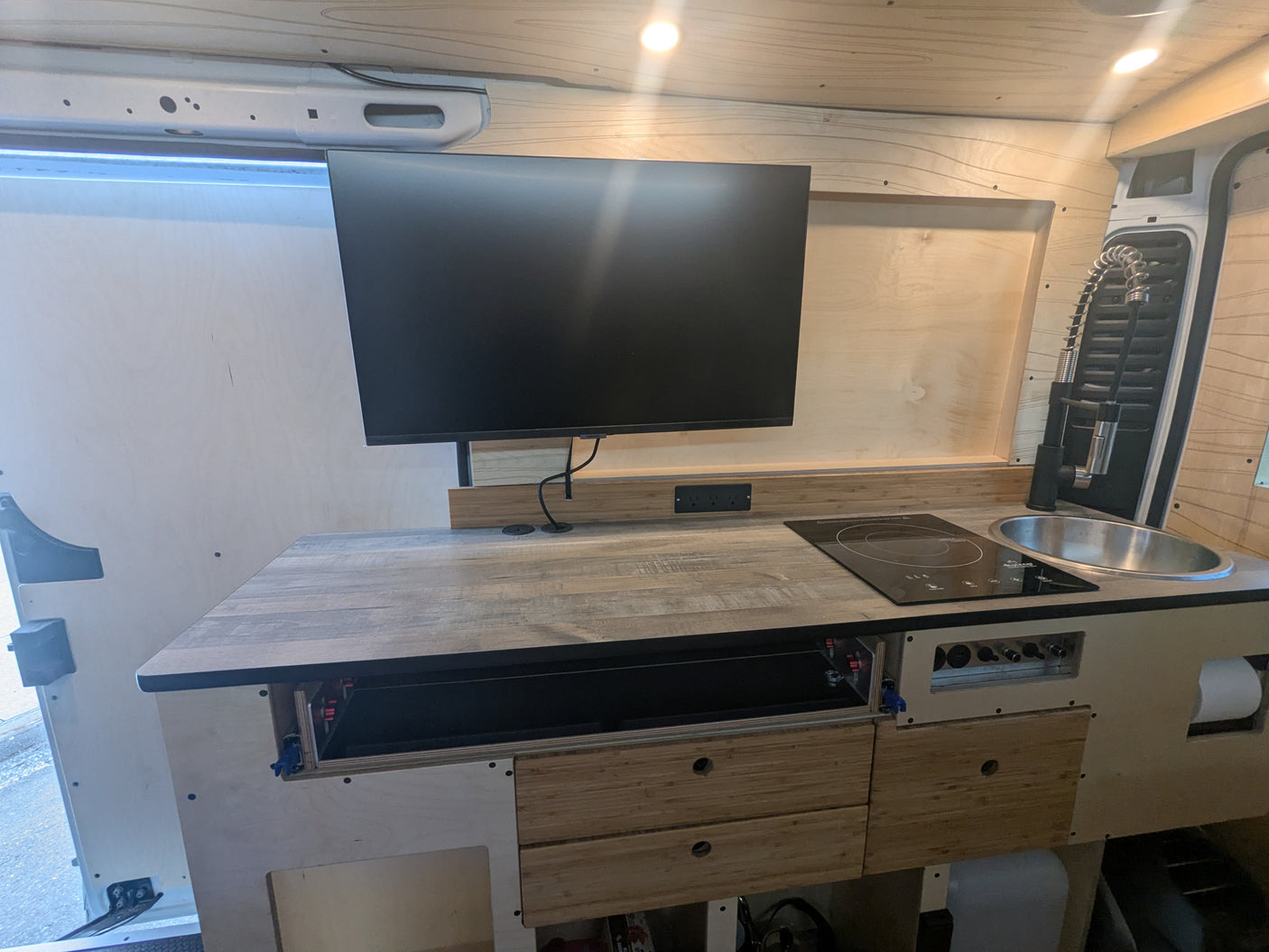 Functional RV rental kitchen area features a monitor, induction cooktop, and sink in a wooden interior.