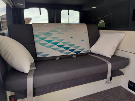 Enjoy comfort in this RV rental! Features a plush bench seat, decorative pillows, and a patterned blanket.