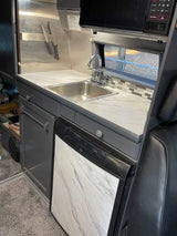 RV rental kitchen with a stainless steel backsplash, sink, microwave, and Dometic fridge with marble-look door.