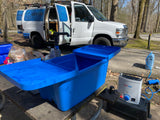 Outdoor camp kitchen setup next to an RV rental van, featuring a portable sink and HOTTAP water heater for convenience.