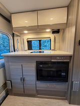 Modern RV rental kitchen featuring a sink, induction cooktop, microwave, and overhead storage with a scenic window view.