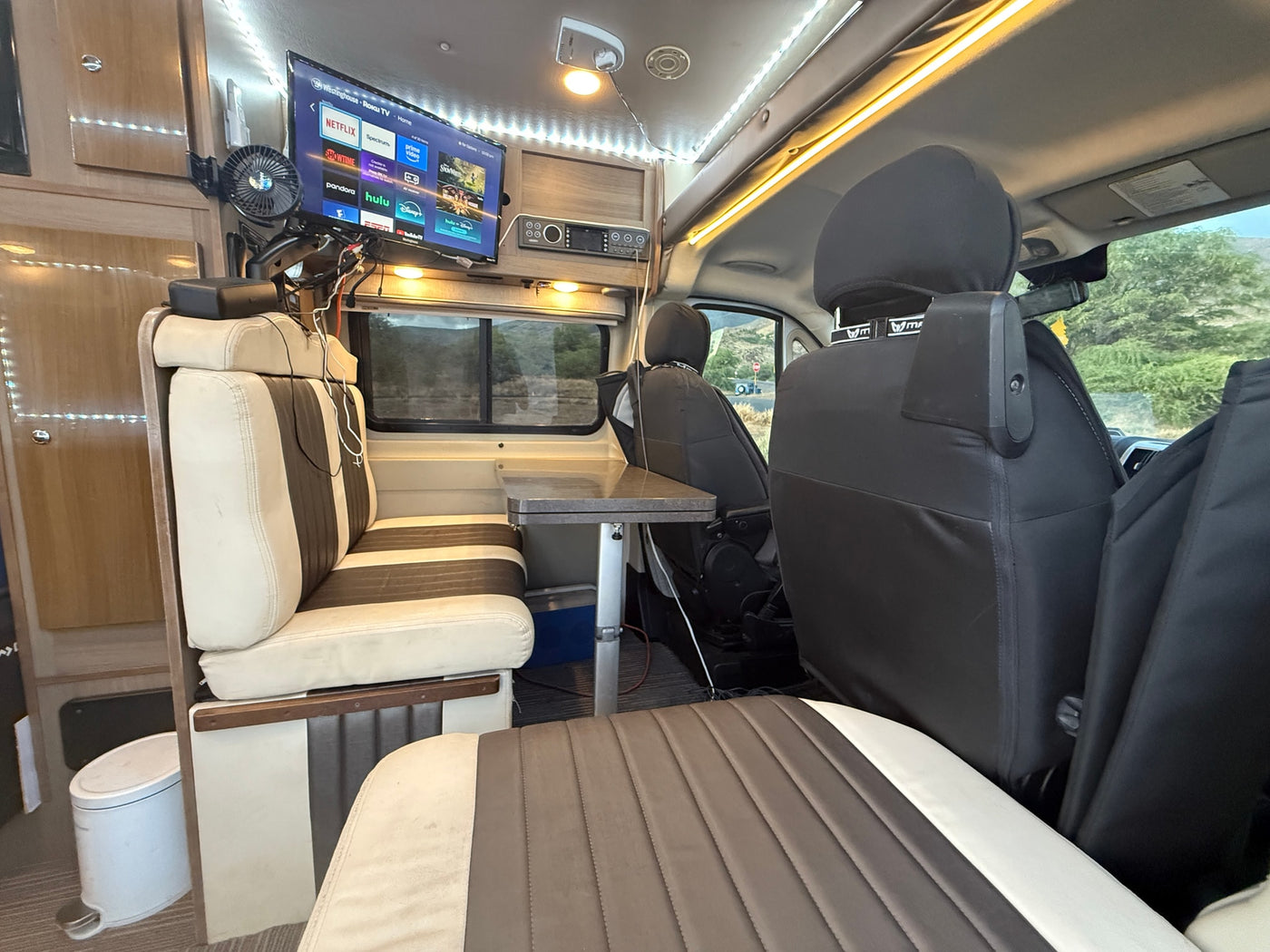 Inside an rv rental: a cozy lounge area with Roku TV, fan, and dining table. Ideal for mobile living & road trips. — photo 6