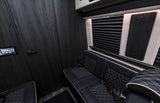 Modern RV rental interior with dark wood walls, quilted leather seats, a control panel, and window blinds.