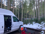White RV rental van parked in a snowy aspen forest, equipped for camping.