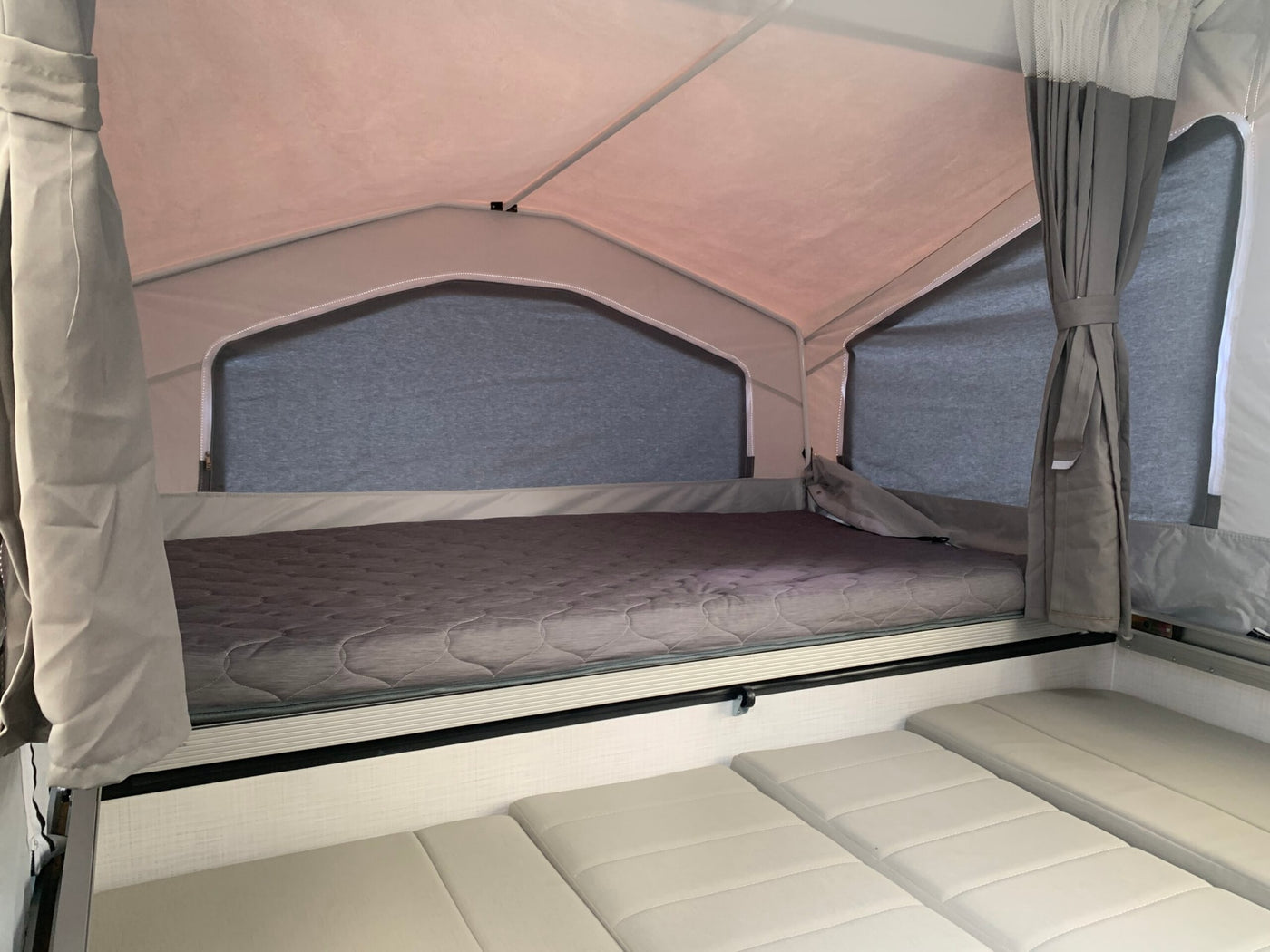 Inside an rv rental pop-up camper: A cozy upper tent-bed with a grey mattress, and versatile lower cushions below. — photo 5