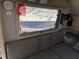 Inside an RV rental: a gray couch, a window offering views of a boat/RV with a solar panel, and a smoke detector.