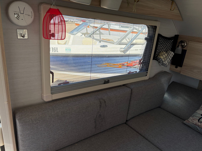 Inside an RV rental: a gray couch, a window offering views of a boat/RV with a solar panel, and a smoke detector. — photo 6