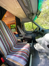 Inside a custom rv rental van with patterned seats, wooden ceiling, and a lush outdoor view. Perfect for van life adventures.