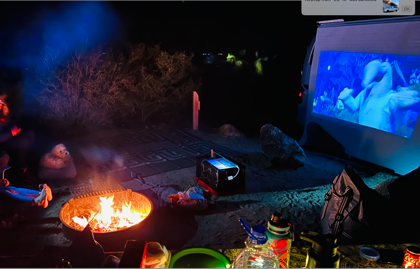 Cozy campfire & outdoor movie night projected on an RV rental screen. Friends relaxing under the stars.