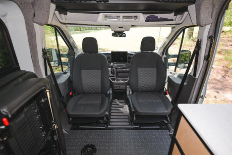 RV rental's front interior: two seats, dashboard, and clear view of an outdoor natural setting.