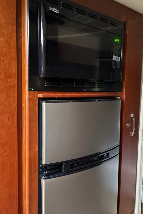 RV rental kitchen: built-in black High Pointe microwave (0:00 green display) & stainless Norcold refrigerator.
