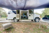 This rv rental camper van is set up for a comfortable outdoor experience with an awning, portable grill, and camp stove.