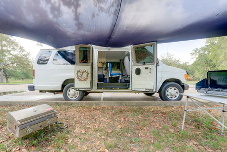 This rv rental camper van is set up for a comfortable outdoor experience with an awning, portable grill, and camp stove.