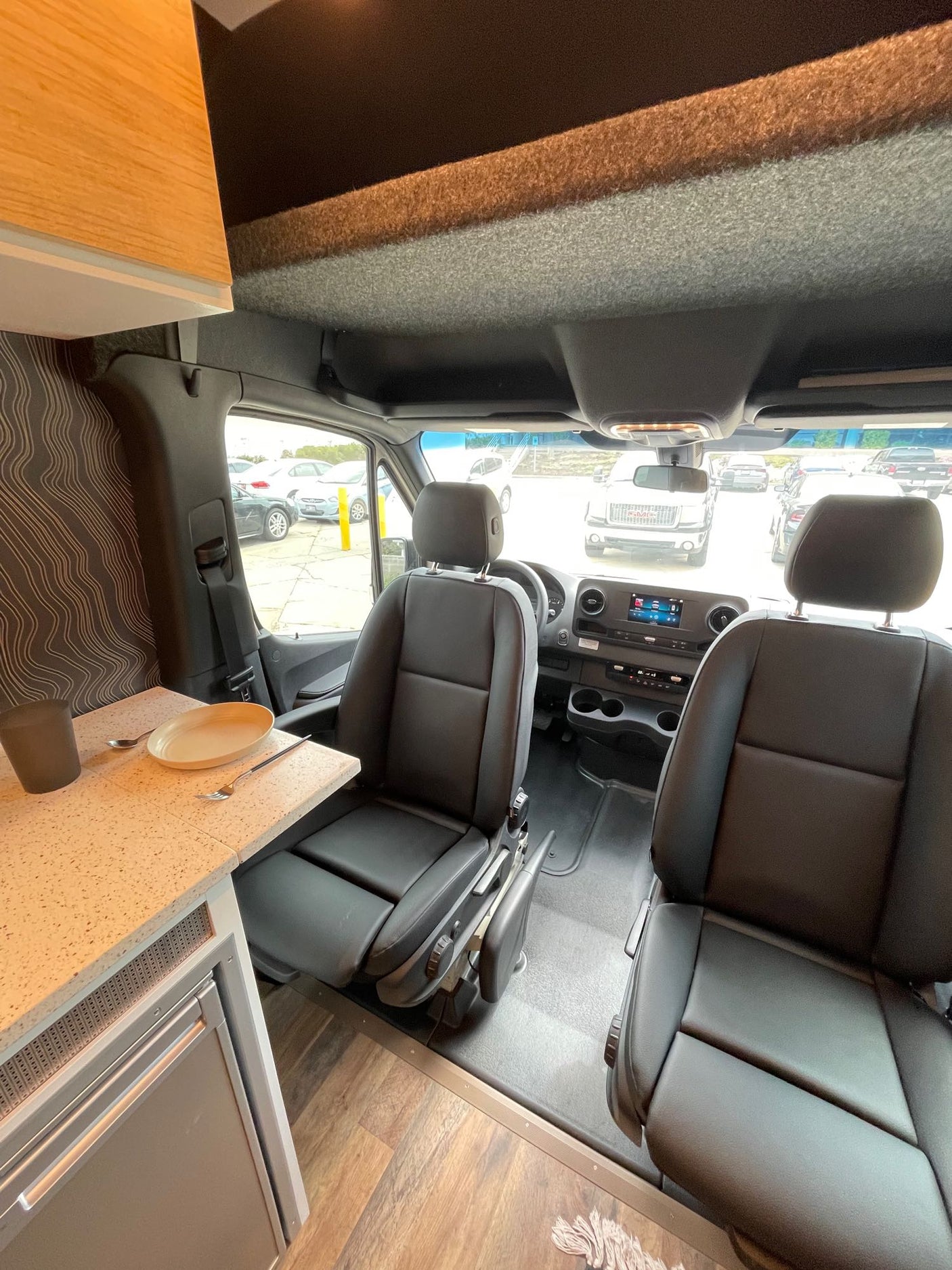 Step inside this RV rental's practical camper van interior: front seats, dashboard, and a compact kitchenette with fridge.