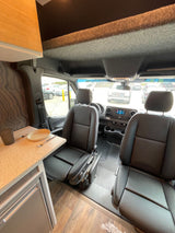 Step inside this RV rental's practical camper van interior: front seats, dashboard, and a compact kitchenette with fridge.