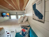 Cozy RV rental interior with a bed, mounted TV, "Never Stop Exploring" pillow, and a California State Parks map.