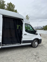 RV rental: White camper van with open mesh-screened door, parked on a gravel riverbank beside a bridge.