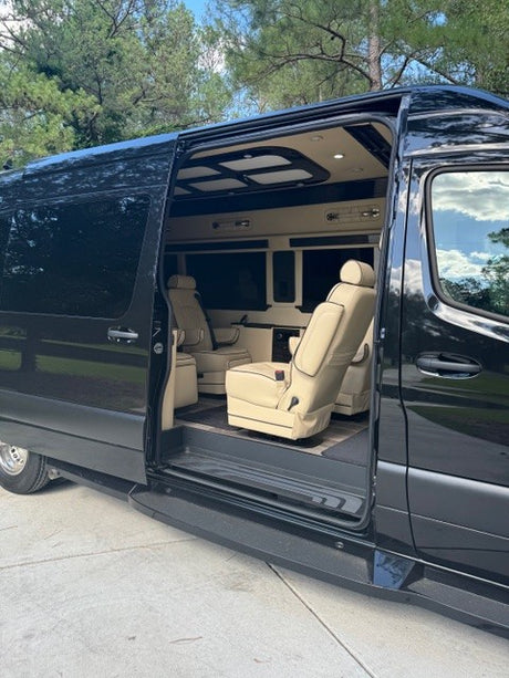 Explore this luxury RV rental's spacious interior! The black van has its side door open, revealing cream, plush captain's chairs.