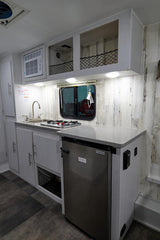 Inside an RV rental: a compact kitchen with a sink, two-burner stove, fridge, and overhead netting storage.