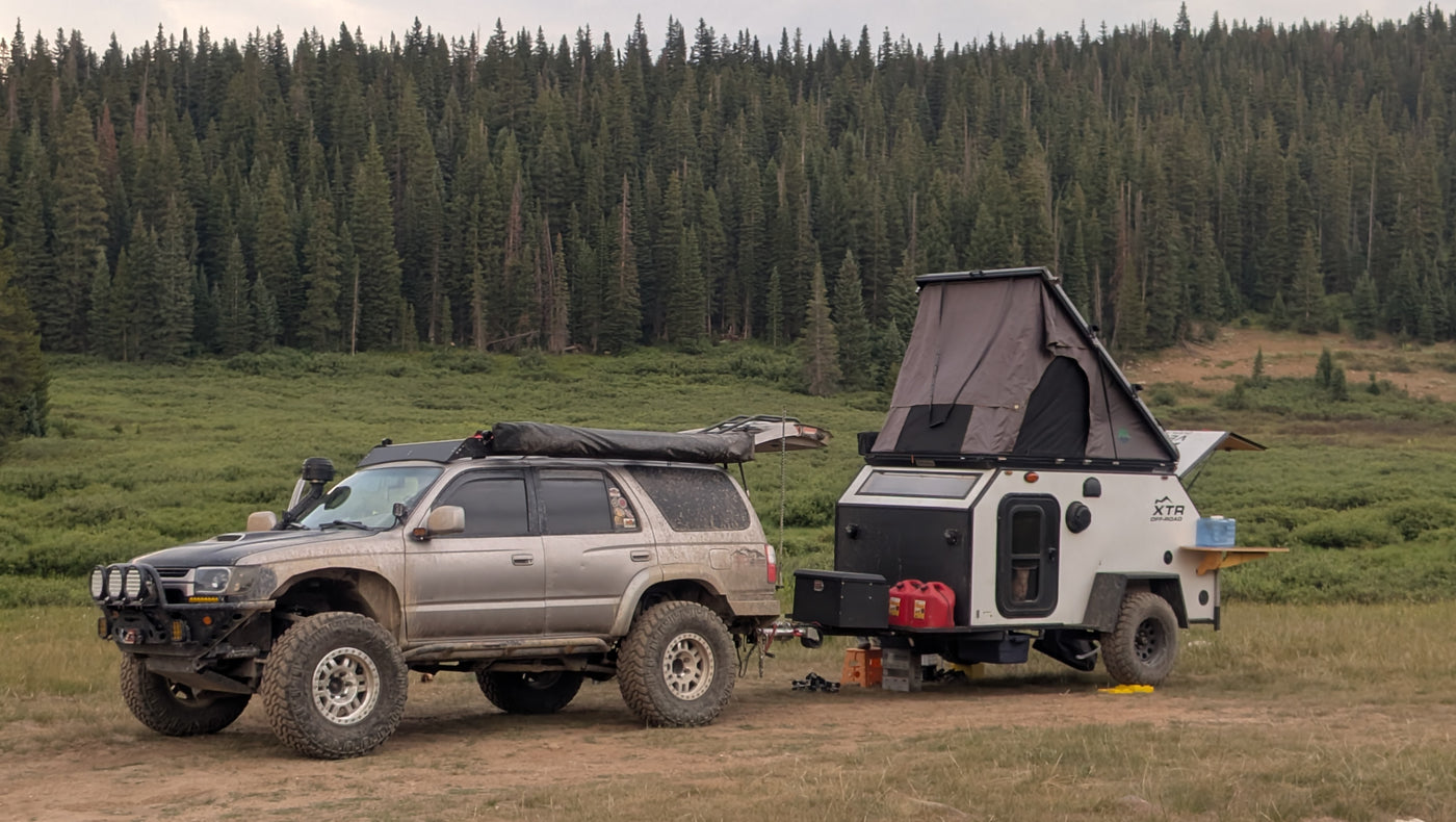 An off-road SUV tows an overlanding trailer with a rooftop tent, parked in a lush forest for a wilderness rv rental adventure. — photo 7