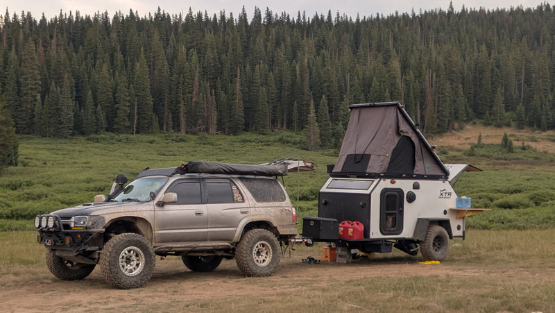 An off-road SUV tows an overlanding trailer with a rooftop tent, parked in a lush forest for a wilderness rv rental adventure. — photo 7