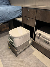Compact RV rental setup features a Dometic portable toilet on a slide, Yeti cooler, and bed for functional living.
