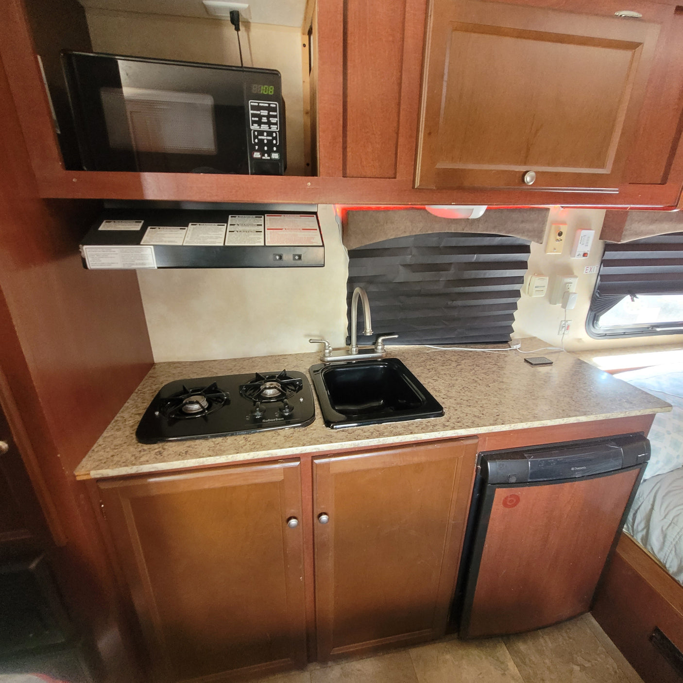 RV rental kitchenette features microwave, gas stove, sink, and compact fridge, ideal for travel.