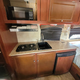 RV rental kitchenette features microwave, gas stove, sink, and compact fridge, ideal for travel.