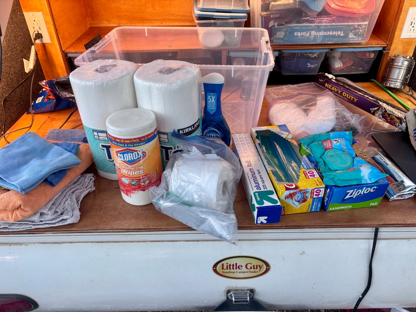 Inside an RV rental, kitchen essentials and cleaning supplies are neatly organized: paper towels, wipes, dish soap, foil, bags. — photo 17