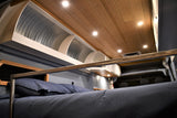 Inside an RV rental: a cozy bed with dark bedding, metal bunk rail, unique curved overhead storage, and wood ceiling.