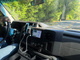 RV rental drive: Navigation on dashboard screen and phone mount. Driver's view of green trees and road ahead.