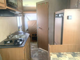 Inside an RV rental: a compact kitchen (stove, sink, microwave), fridge, and bed area, designed for efficient living.