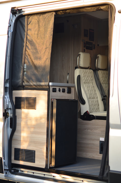 Overhead view of a modern RV rental interior, showing kitchen area with fridge, control panel, and plush seating for comfortable travel.