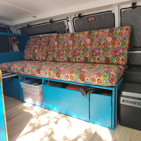 Colorful RV rental interior featuring vibrant cushions, blue built-in storage, and a floor cooler for comfortable travel.