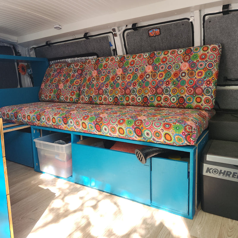 Colorful RV rental interior featuring vibrant cushions, blue built-in storage, and a floor cooler for comfortable travel. — photo 11