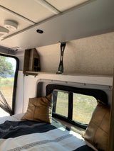 Cozy RV rental interior showing a comfortable bed, overhead storage, and a window with nature views, perfect for travel.