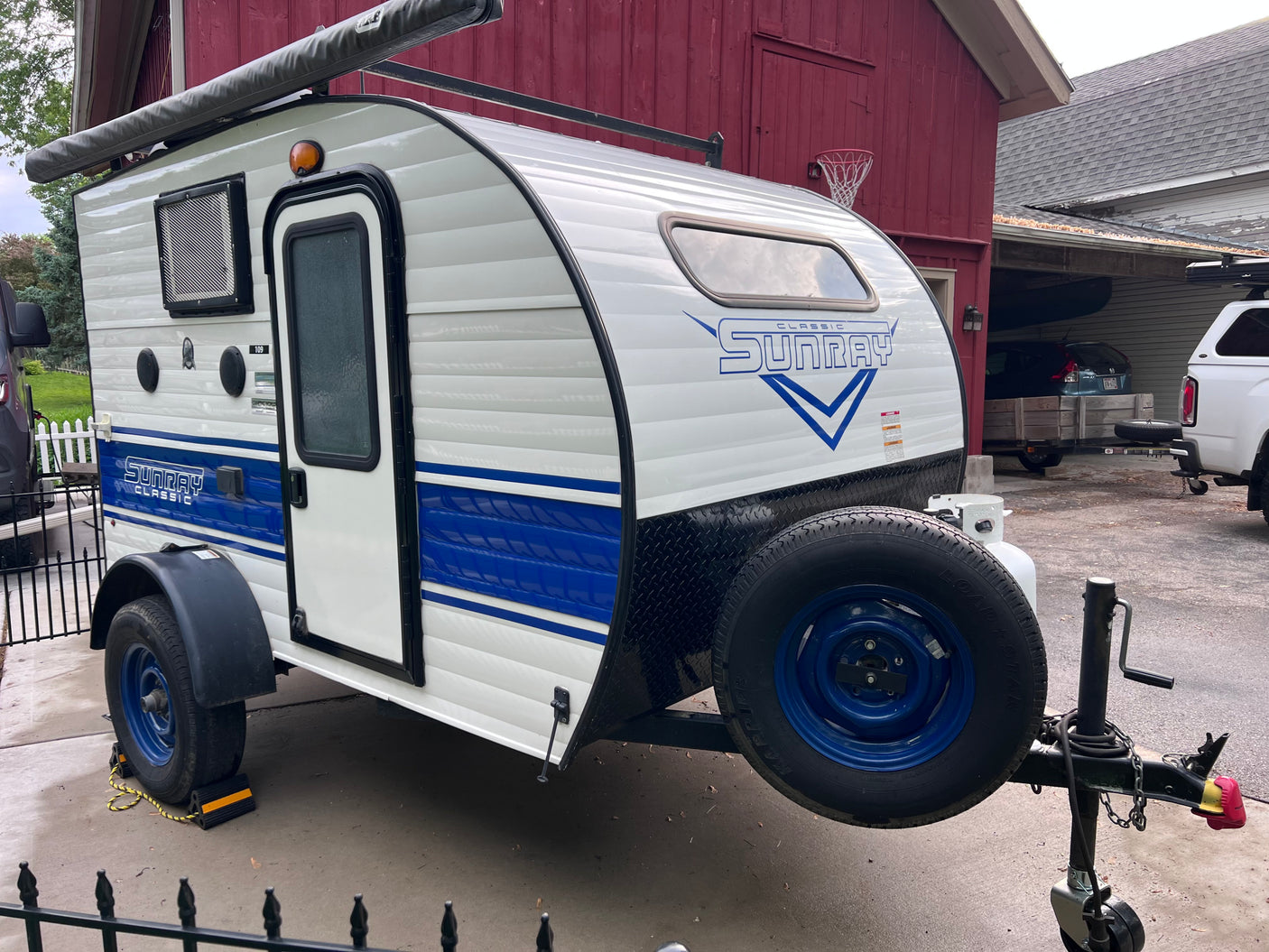 A white and blue Sunray Classic teardrop camper, seen parked, would make a great RV rental for camping.