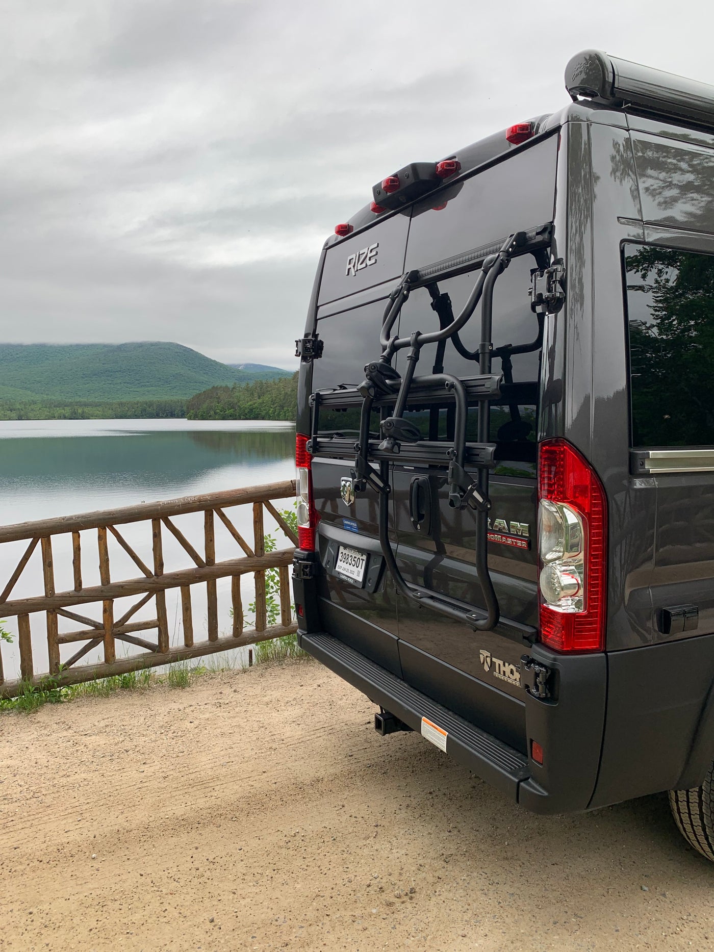 Dark gray Rize camper van with a bike rack by a scenic lake and mountains, perfect for an RV rental outdoor adventure. — photo 4