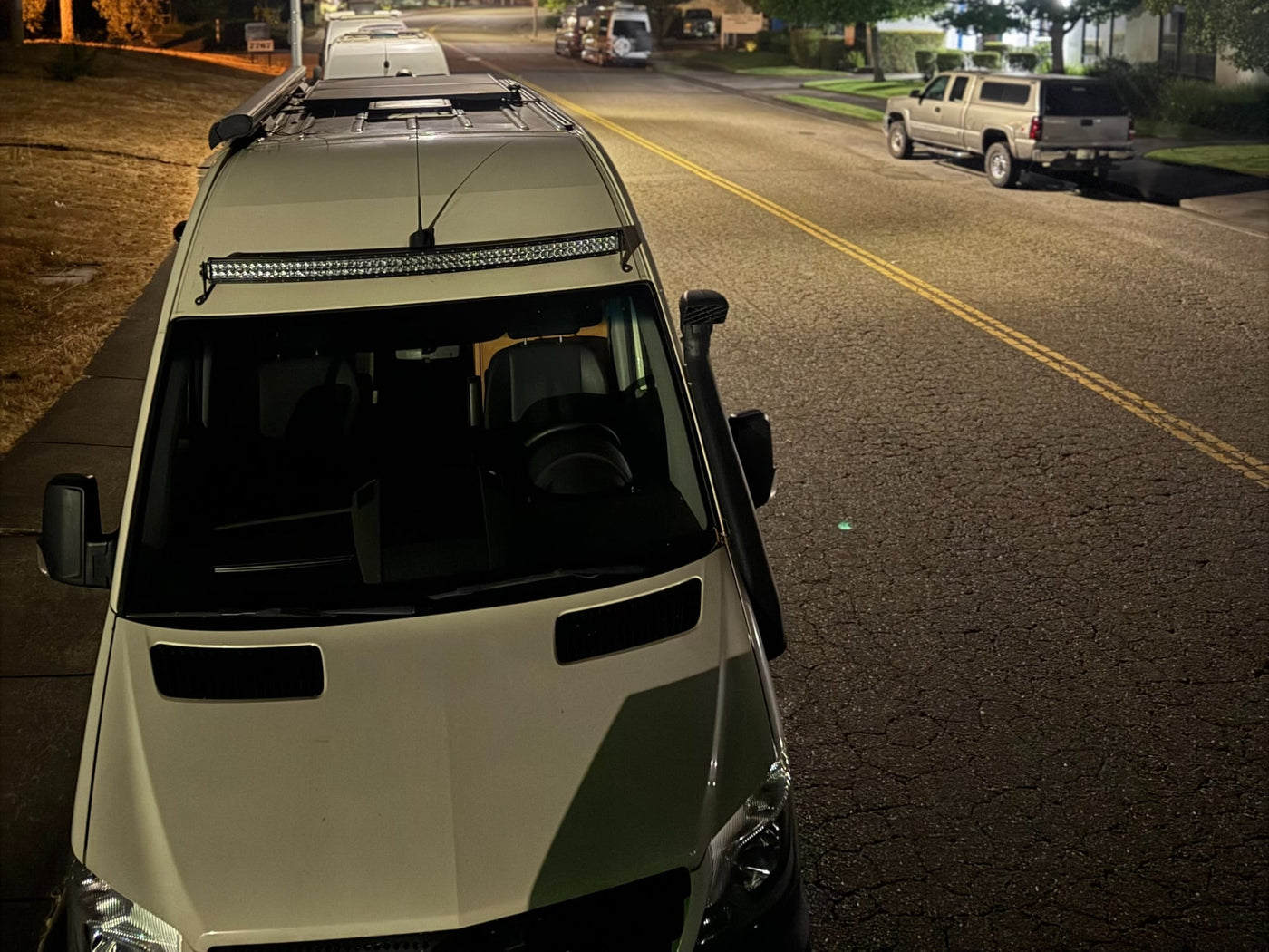A dog watches a gray RV rental parked in a cloudy lot with trees and a "J4 PARKING" sign visible on a lamppost.|A dark grey RV rental van is parked in a lot — photo 5