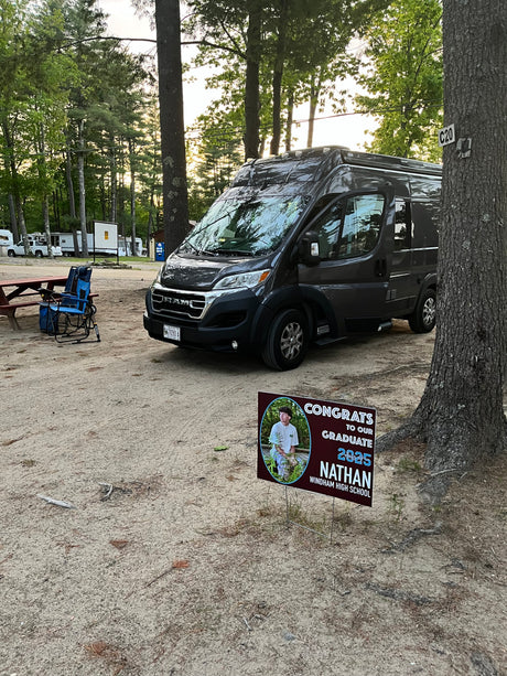 Dark grey RV rental at C20 campsite, next to a picnic table. A yard sign congratulates Nathan, Windham High School Class of 2025.