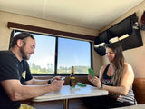 A couple enjoys playing cards and a beer inside their RV rental, with a scenic view through the window. Perfect for RV travel.
