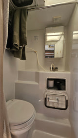Compact RV rental bathroom with a toilet, sink, shower, and integrated storage visible, offering functional space.
