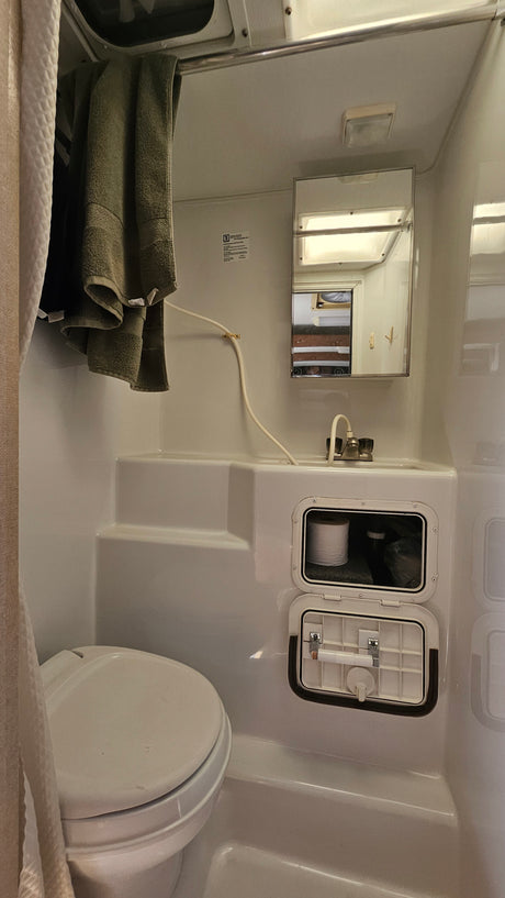 Compact RV rental bathroom with a toilet, sink, shower, and integrated storage visible, offering functional space.
