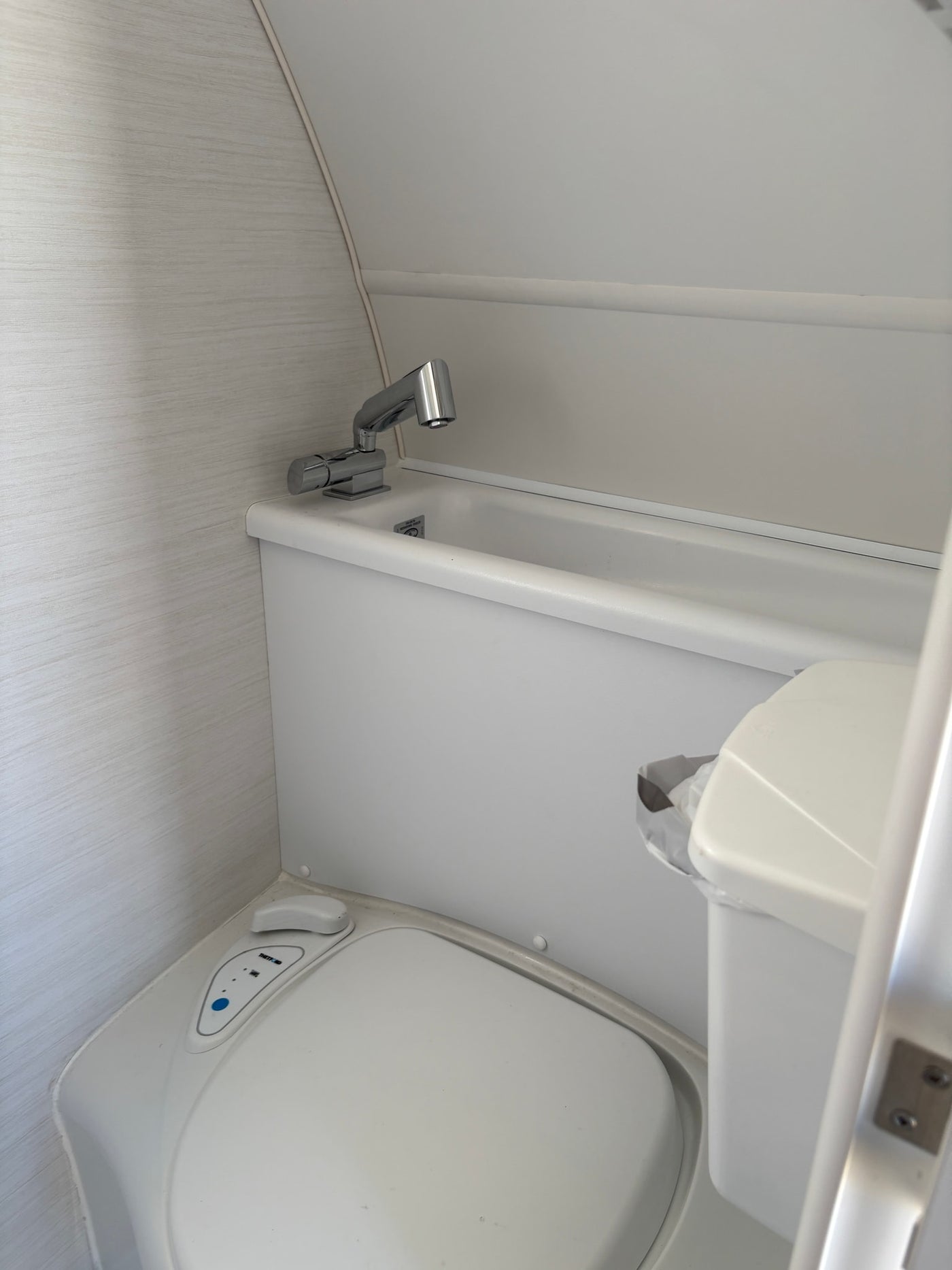 Compact bathroom in an RV rental, featuring a white toilet, integrated sink with chrome faucet, and small bin. — photo 8