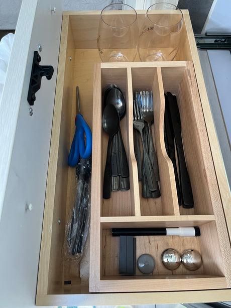 RV rental kitchen drawer, neatly organized with stemless glasses, black utensils, scissors, and a marker in a wooden insert.