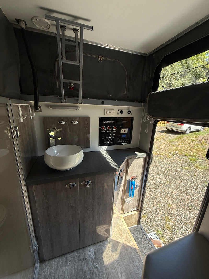 Cabin interior looking toward the vanity and control panel, with the roof ladder stowed overhead and the door open to the campsite — photo 11