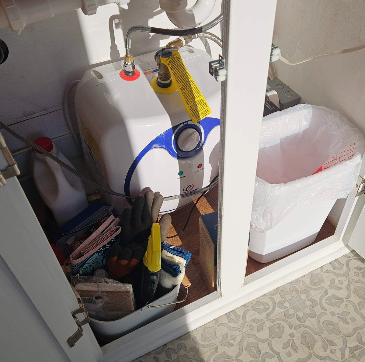 Organized RV rental under-sink storage: features a compact water heater, trash bin, and cleaning supplies. Essential for tiny living. — photo 13