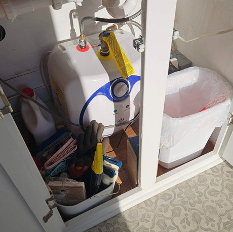 Organized RV rental under-sink storage: features a compact water heater, trash bin, and cleaning supplies. Essential for tiny living.