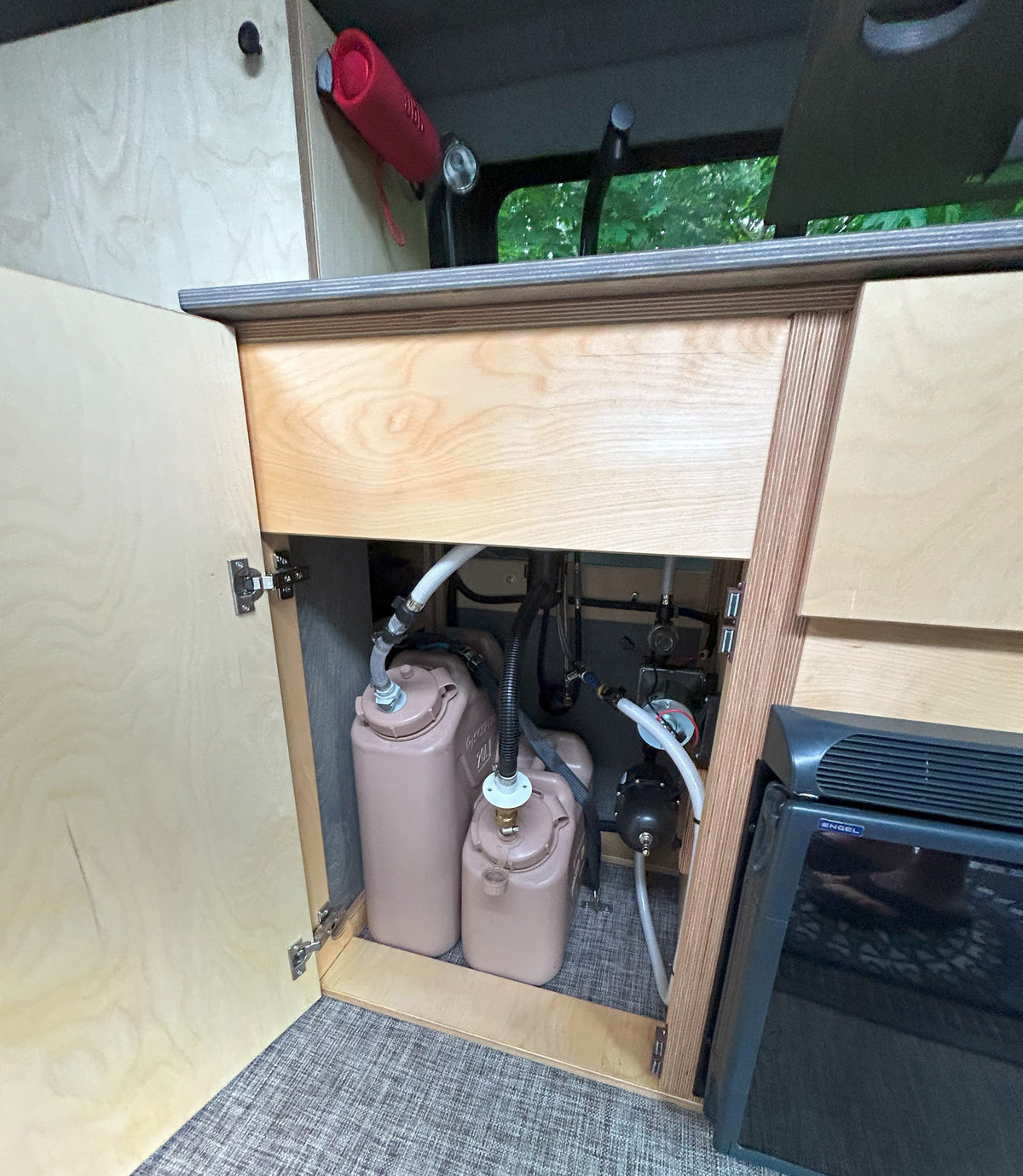 **RV rental** water system: portable tanks, pump, and fridge inside a camper kitchen. — photo 11
